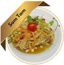 A plate of Som Tam (Thai papaya salad) garnished with cherry tomato, peanuts, and fresh herbs, displayed with a golden ribbon label reading "Som Tam."